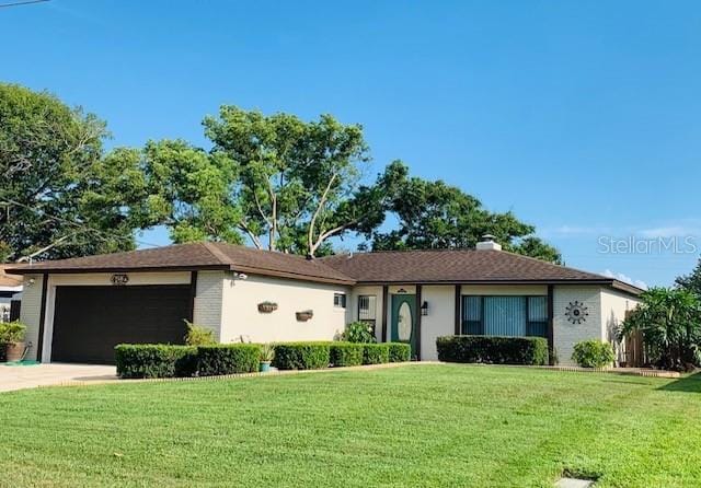 ranch-style home with an attached garage, brick siding, driveway, a front lawn, and a chimney