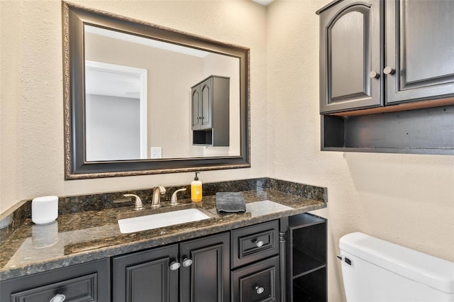 bathroom with toilet, a textured wall, and vanity