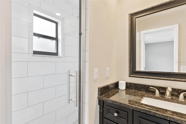 bathroom with a textured wall, a shower stall, and vanity