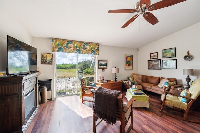 living area featuring a ceiling fan, vaulted ceiling, wood finished floors, and a glass covered fireplace