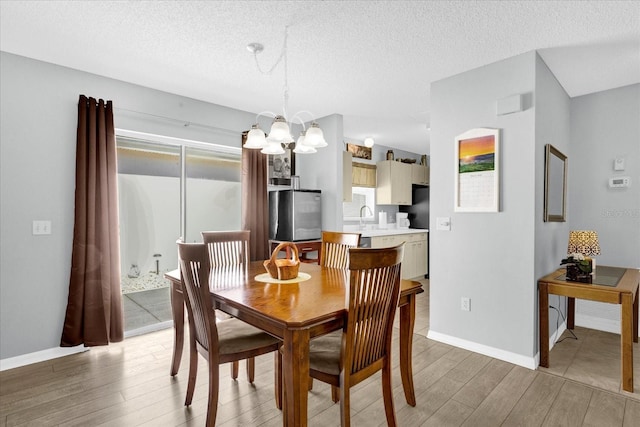 dining area featuring a chandelier, a textured ceiling, baseboards, and light wood-style floors