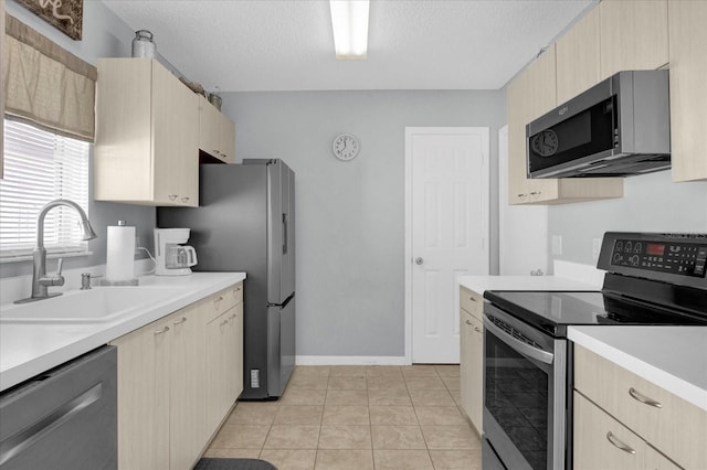 kitchen featuring stainless steel appliances, a textured ceiling, light brown cabinetry, light countertops, and a sink