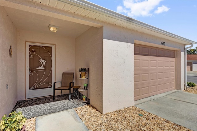 doorway to property featuring a garage, driveway, and stucco siding