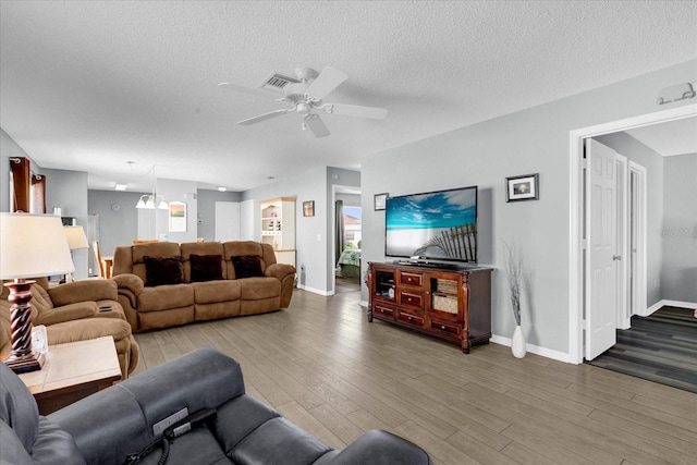 living area with a textured ceiling, wood finished floors, visible vents, baseboards, and a ceiling fan