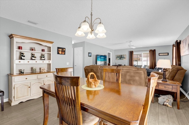 dining room featuring light wood-style floors, visible vents, a textured ceiling, and ceiling fan with notable chandelier