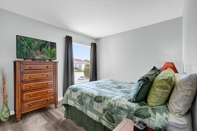 bedroom with a textured ceiling, baseboards, and wood finished floors