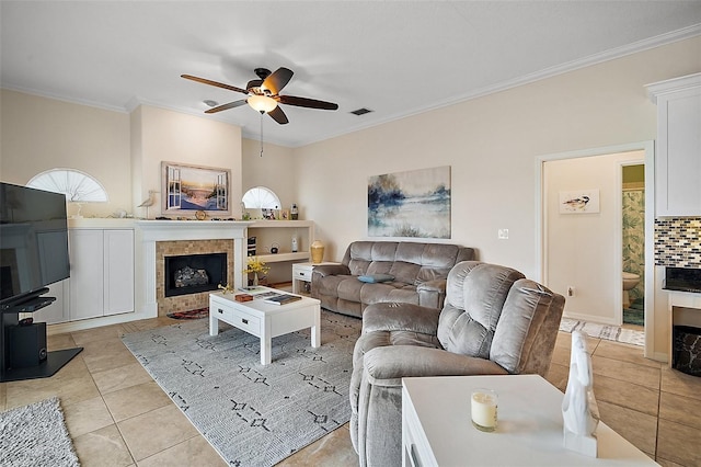 living area featuring a ceiling fan, ornamental molding, a tiled fireplace, and light tile patterned floors