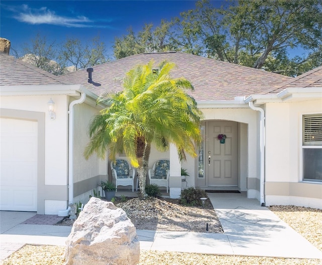 entrance to property with a garage, a shingled roof, covered porch, and stucco siding