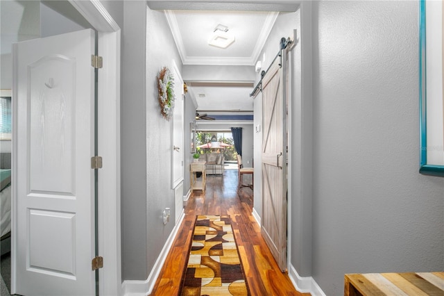 hallway with wood finished floors, baseboards, crown molding, a barn door, and a textured wall