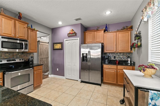 kitchen featuring tasteful backsplash, visible vents, a barn door, light tile patterned floors, and stainless steel appliances