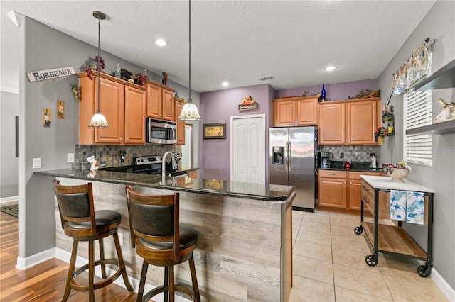 kitchen with visible vents, pendant lighting, stainless steel appliances, a peninsula, and light tile patterned floors