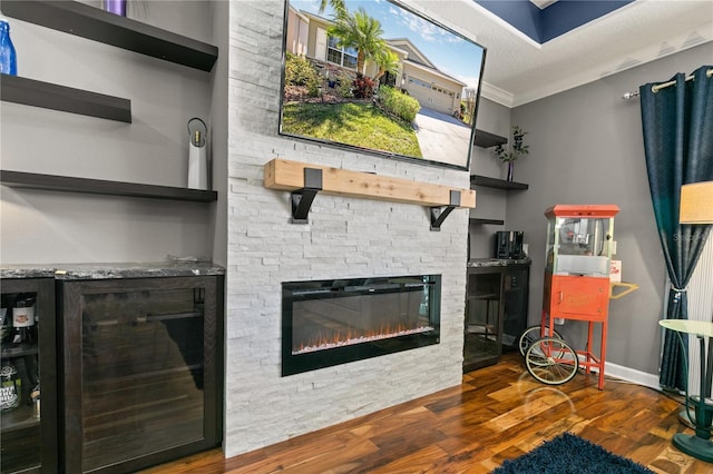 living area featuring beverage cooler, ornamental molding, a textured ceiling, wood finished floors, and a stone fireplace