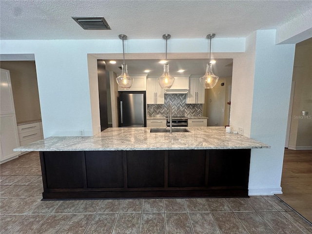 kitchen featuring visible vents, decorative backsplash, white cabinetry, a sink, and stainless steel refrigerator