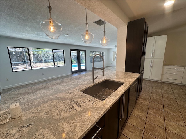 kitchen with french doors, visible vents, hanging light fixtures, a sink, and light stone countertops