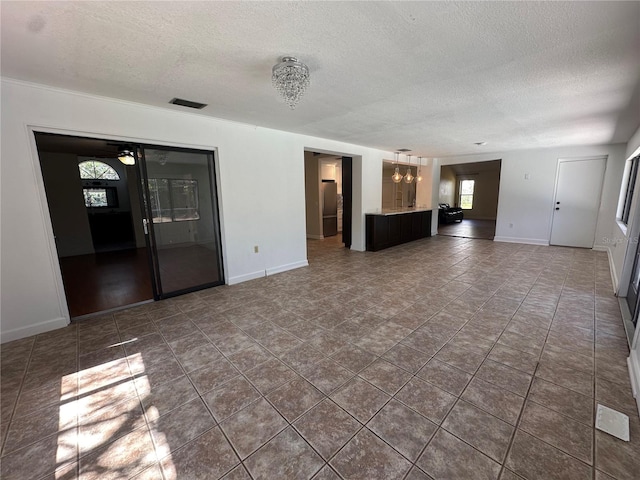 unfurnished living room with visible vents, a notable chandelier, a textured ceiling, and baseboards