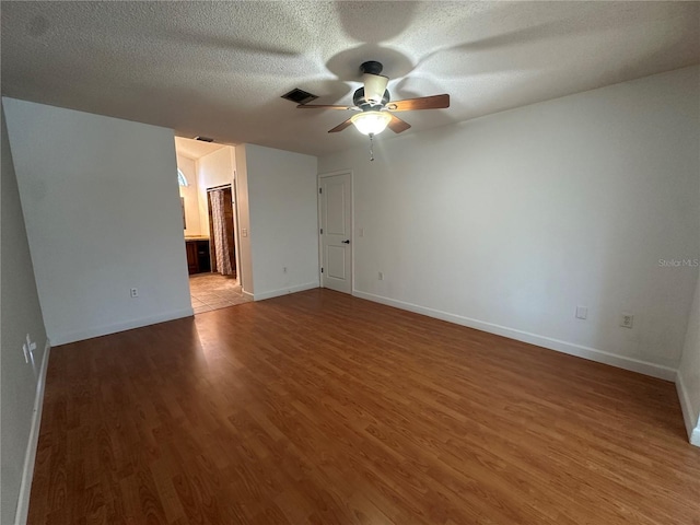 unfurnished room featuring baseboards, visible vents, ceiling fan, wood finished floors, and a textured ceiling