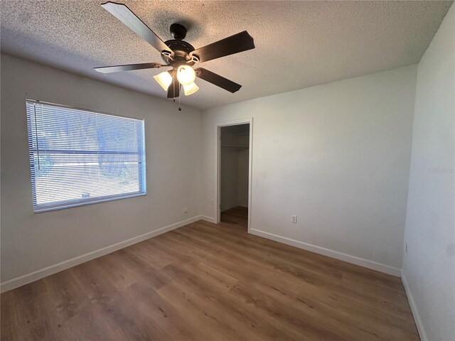 unfurnished bedroom featuring a ceiling fan, a textured ceiling, baseboards, and wood finished floors