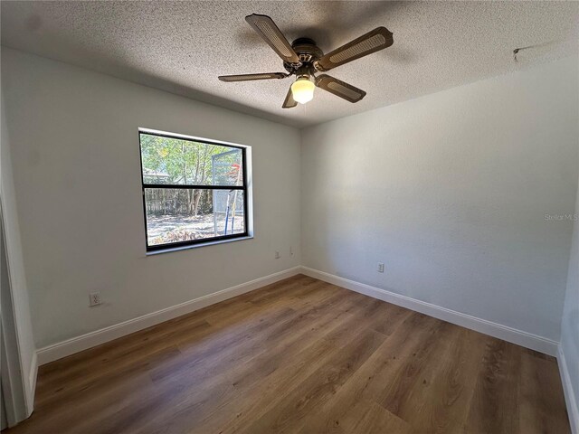 empty room with a textured ceiling, baseboards, and wood finished floors