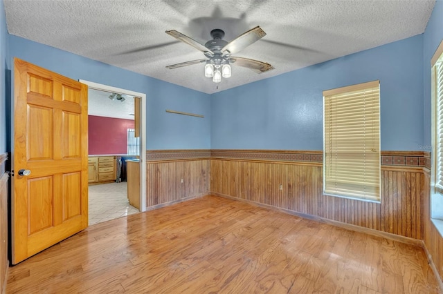 empty room featuring wood finished floors, a wainscoted wall, ceiling fan, wood walls, and a textured ceiling