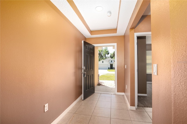 foyer entrance with a tray ceiling, light tile patterned floors, and baseboards