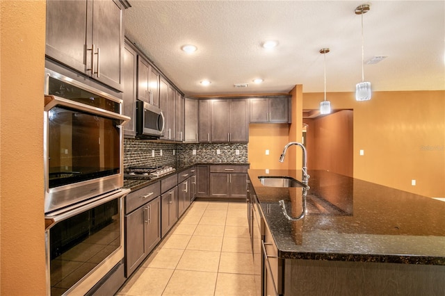 kitchen featuring a sink, dark stone countertops, backsplash, appliances with stainless steel finishes, and light tile patterned floors