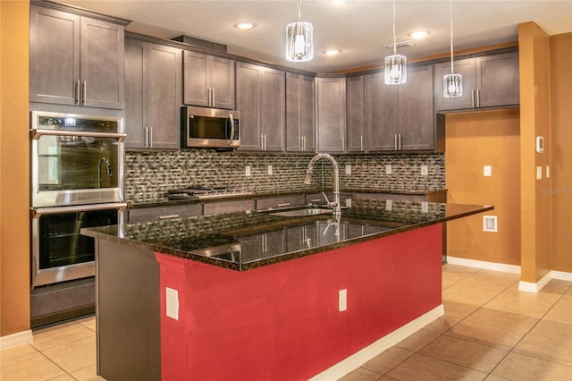 kitchen featuring light tile patterned floors, decorative backsplash, dark stone countertops, appliances with stainless steel finishes, and a sink