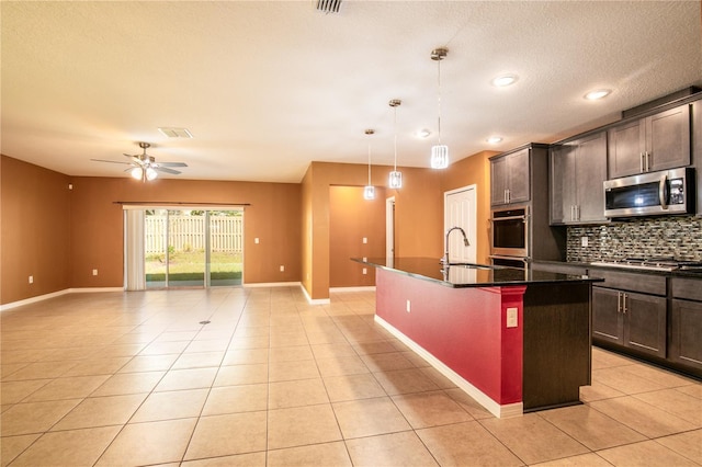 kitchen with light tile patterned floors, an island with sink, a sink, appliances with stainless steel finishes, and open floor plan