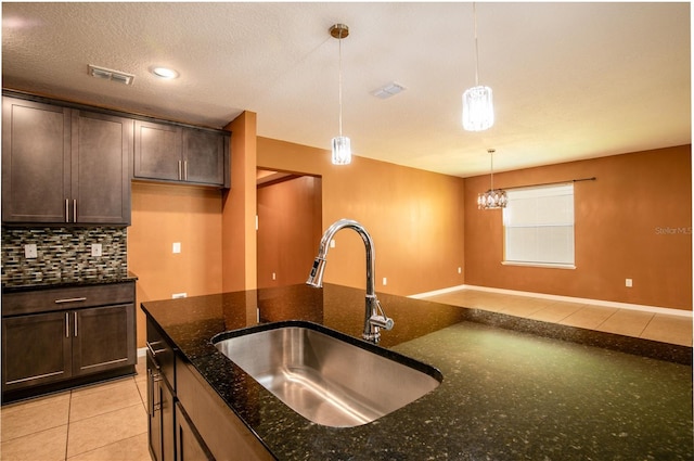 kitchen featuring dark brown cabinetry, decorative light fixtures, backsplash, and a sink