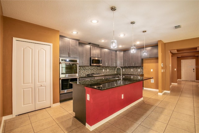 kitchen with dark stone countertops, visible vents, light tile patterned flooring, stainless steel appliances, and backsplash