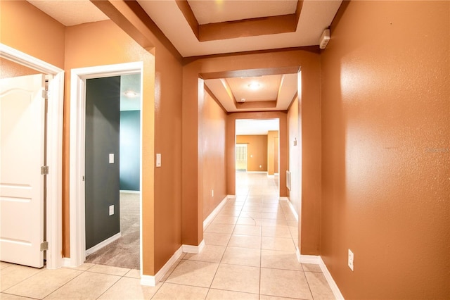 hallway with light tile patterned flooring, baseboards, and a tray ceiling