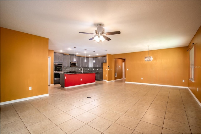 unfurnished living room featuring light tile patterned flooring, ceiling fan with notable chandelier, baseboards, and a sink