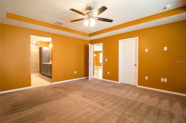 unfurnished bedroom with baseboards, visible vents, ensuite bath, a textured ceiling, and light carpet