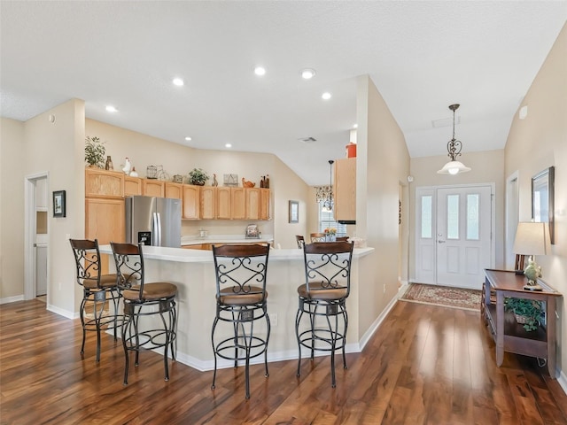 kitchen with a breakfast bar, dark wood finished floors, stainless steel refrigerator with ice dispenser, lofted ceiling, and a peninsula