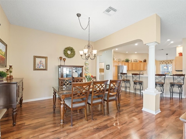 dining room with visible vents, light wood-style floors, baseboards, decorative columns, and an inviting chandelier