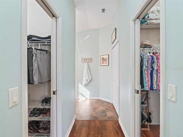 hallway with baseboards, a textured ceiling, visible vents, and dark wood-type flooring