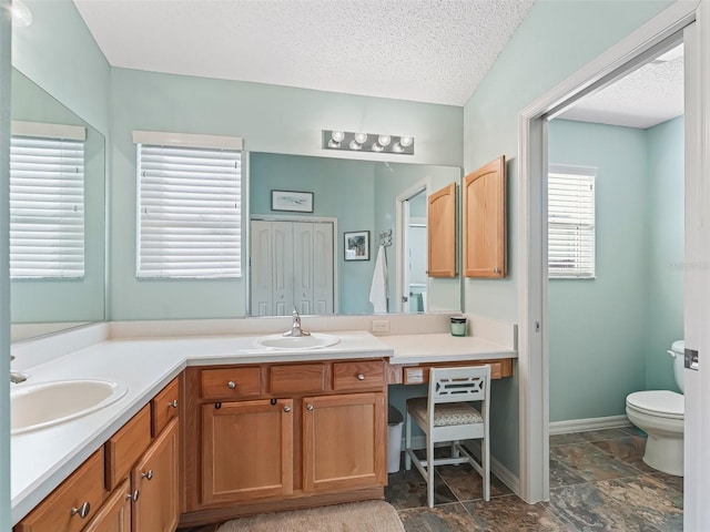 full bathroom featuring double vanity, a textured ceiling, toilet, and a sink