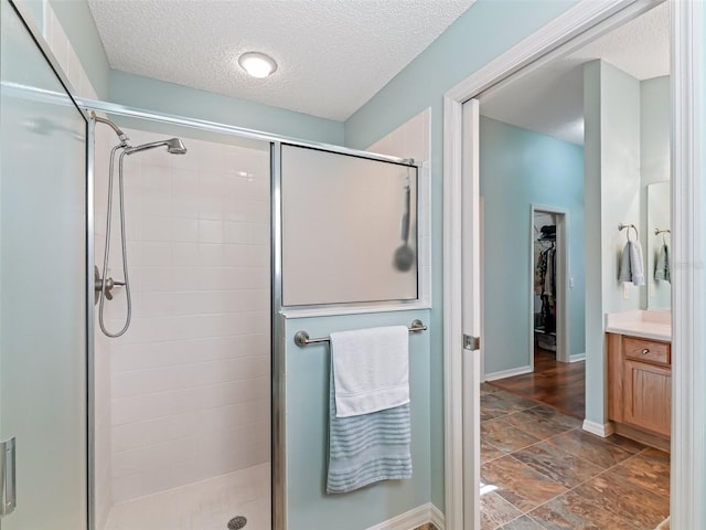 bathroom with a textured ceiling, vanity, baseboards, a spacious closet, and a shower stall