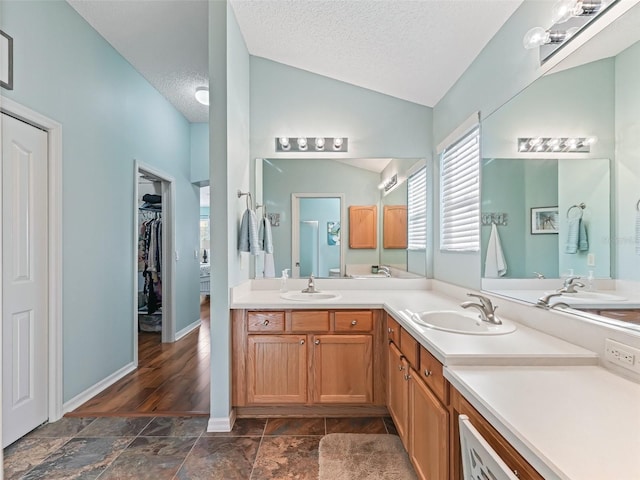 full bathroom with double vanity, a textured ceiling, vaulted ceiling, and a sink