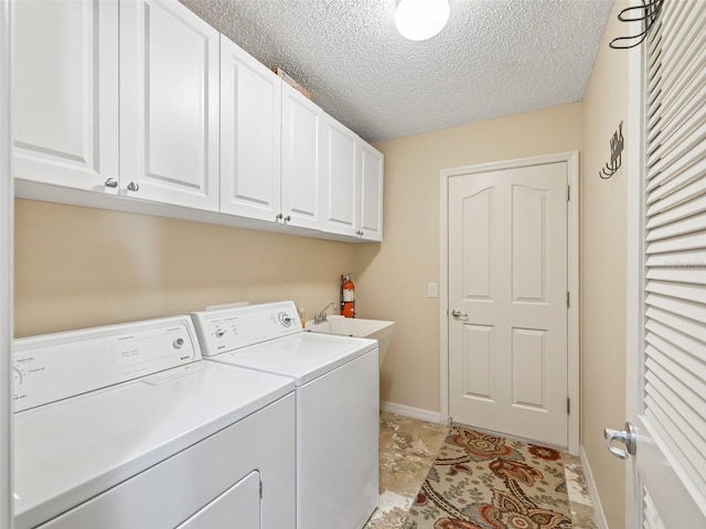 washroom featuring cabinet space, baseboards, washing machine and clothes dryer, a textured ceiling, and a sink