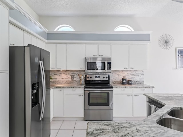 kitchen featuring a textured ceiling, light stone counters, white cabinetry, appliances with stainless steel finishes, and decorative backsplash