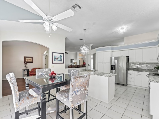 dining area featuring arched walkways, lofted ceiling, light tile patterned flooring, visible vents, and a ceiling fan