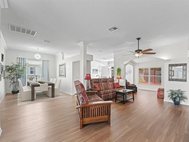 living area with ceiling fan with notable chandelier, visible vents, a textured ceiling, and wood finished floors