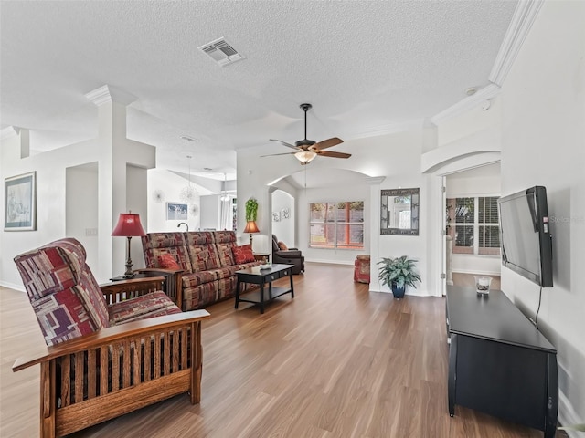 living room featuring light wood finished floors, a ceiling fan, visible vents, and crown molding