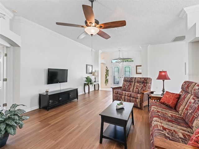 living area with a textured ceiling, wood finished floors, visible vents, french doors, and ornamental molding