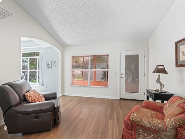 sitting room with a textured ceiling, baseboards, vaulted ceiling, and wood finished floors