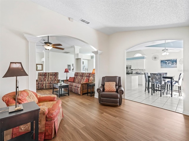 living room featuring ceiling fan, decorative columns, visible vents, and light wood-style flooring