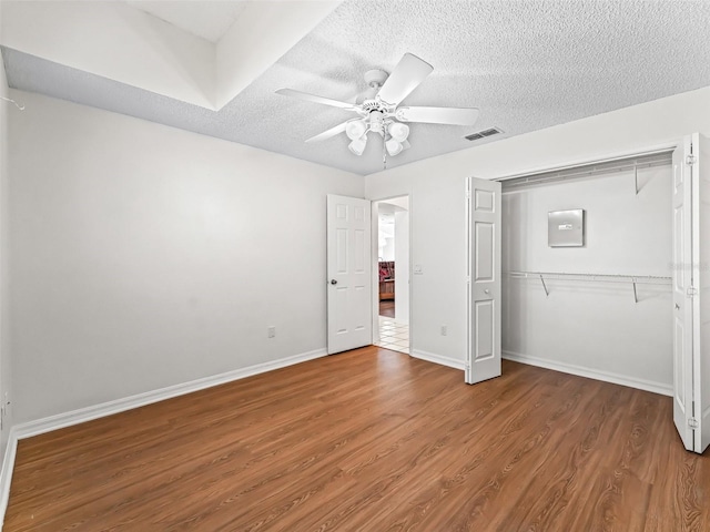 unfurnished bedroom with a textured ceiling, wood finished floors, visible vents, baseboards, and a closet