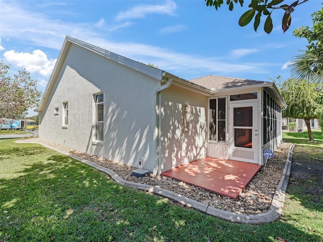 rear view of property with a shingled roof, a sunroom, a lawn, and stucco siding