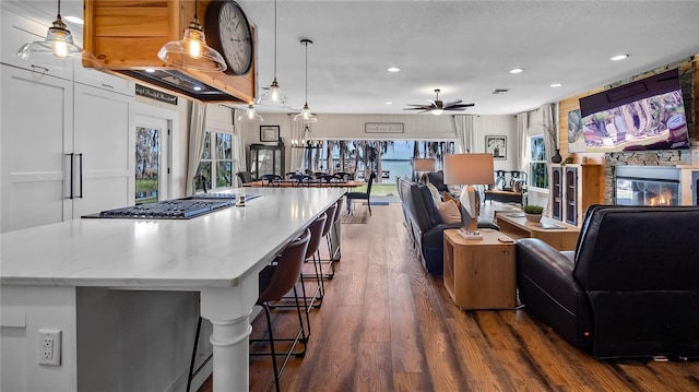 kitchen featuring dark wood-type flooring, a fireplace, a ceiling fan, and pendant lighting