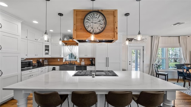 kitchen with visible vents, stainless steel microwave, a kitchen bar, white cabinetry, and gas cooktop